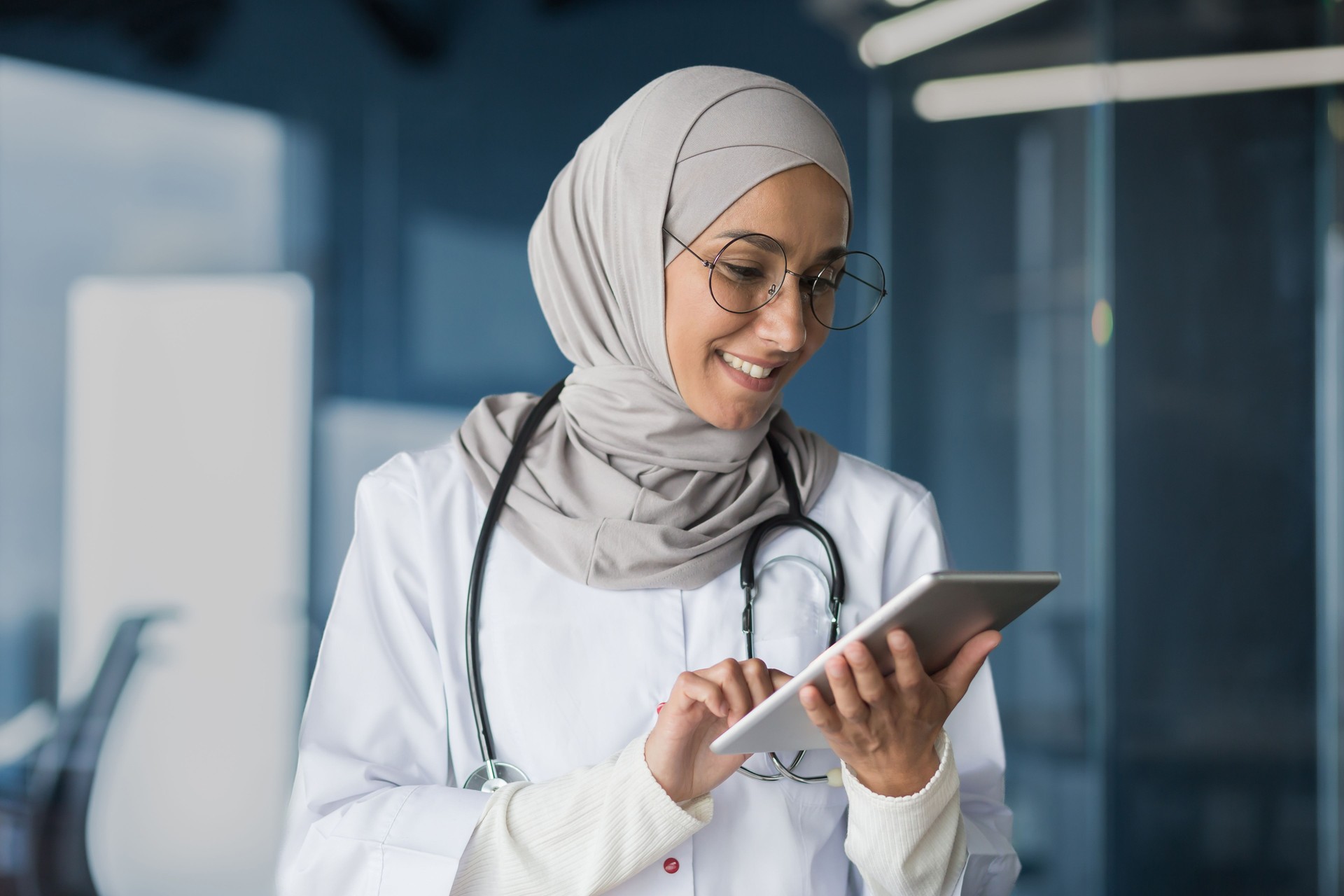 Female doctor in hijab works in modern clinic office, Muslim female doctor uses tablet computer, nurse in medical white coat and glasses with stethoscope