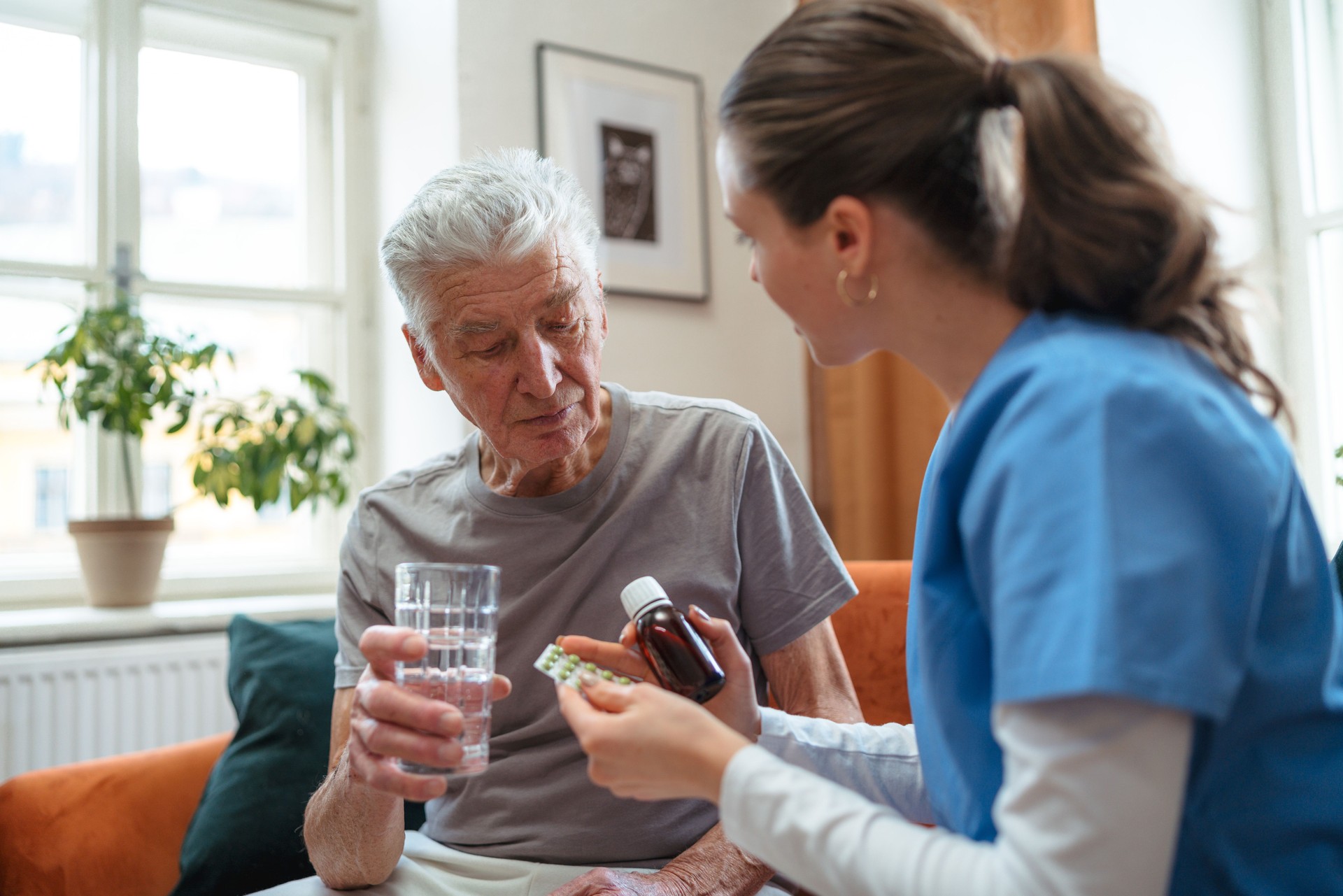 Nurse giving pills senior man in his home.