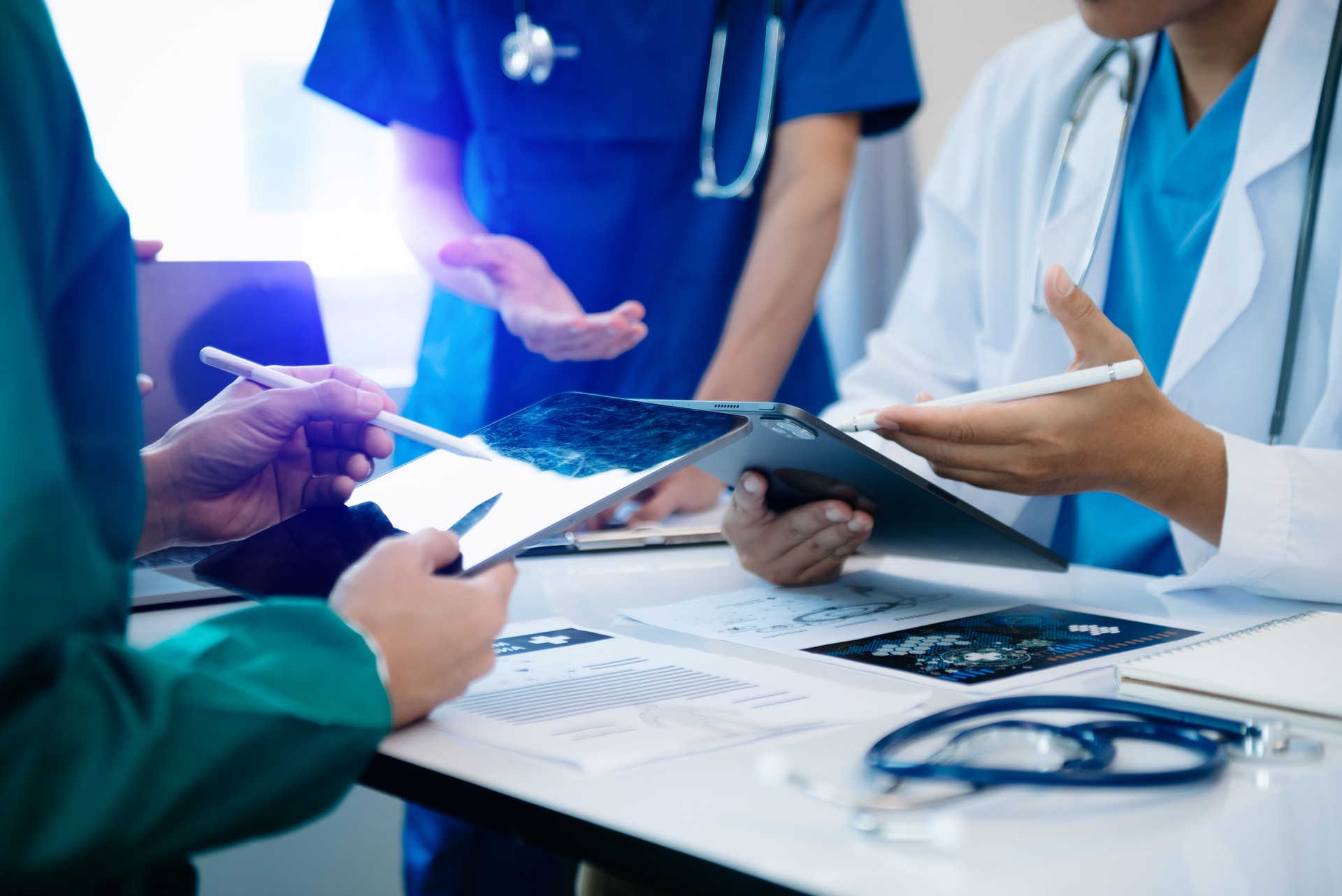 Medical team having a meeting with doctors in white lab coats and surgical scrubs seated at a table discussing a patients working online using computers