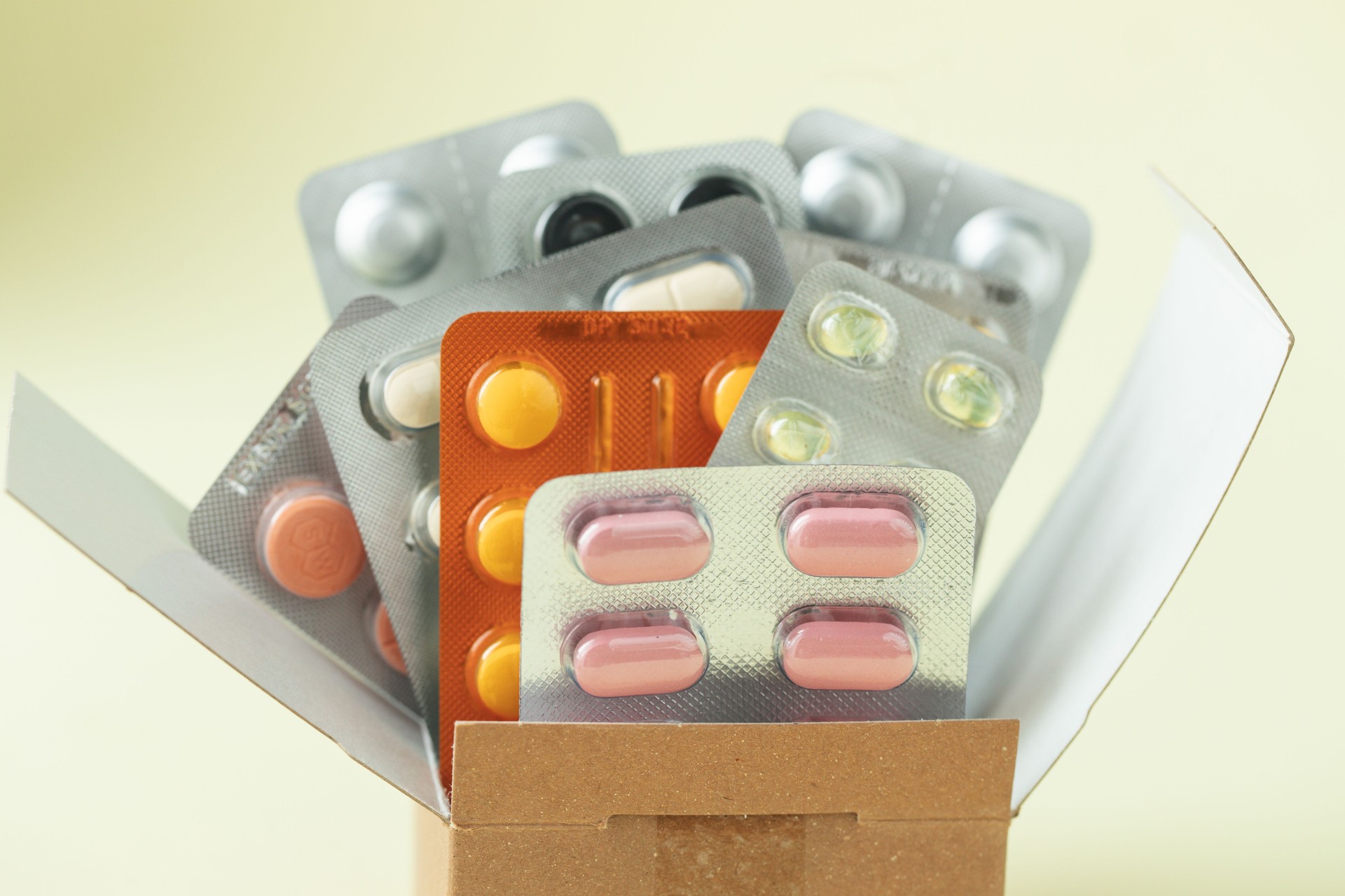 Online medical shopping, home delivery of medicines from the pharmacy. Health concept, cardboard box with pills, medicines, bottles, injections isolated on yellow background