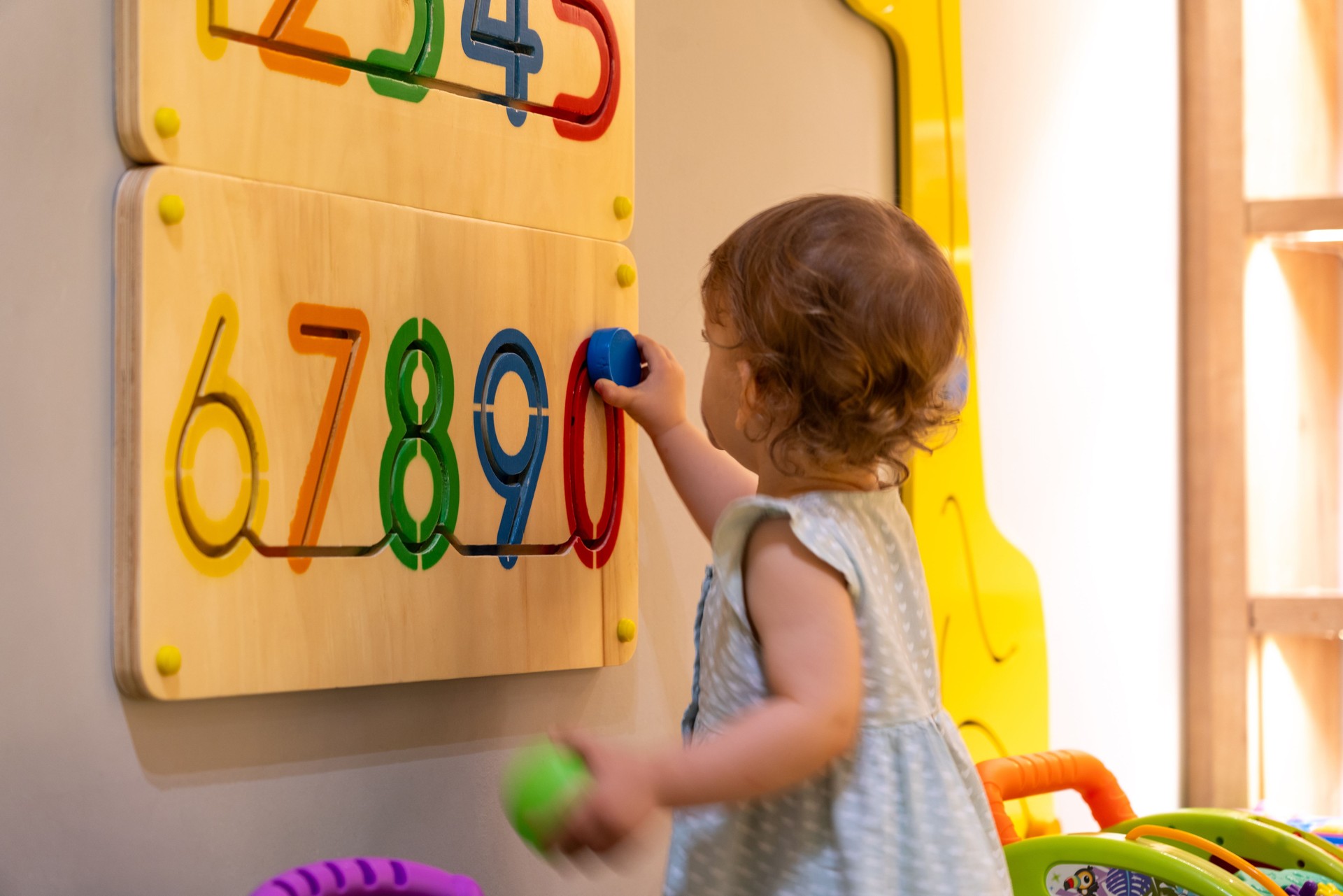 Toddler girl playing with busy board with numbers on the wall. Educational toys. Busy board for children. Wooden game board with numbers